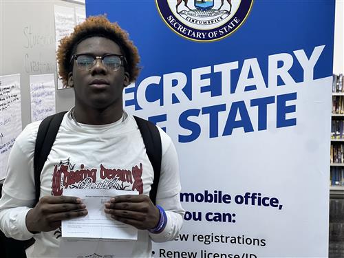 student standing next to Secretary of State banner holding documents